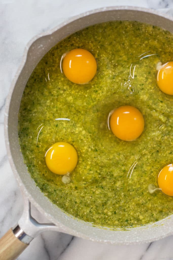 Overhead view of a skillet with raw eggs on top of a green sauce