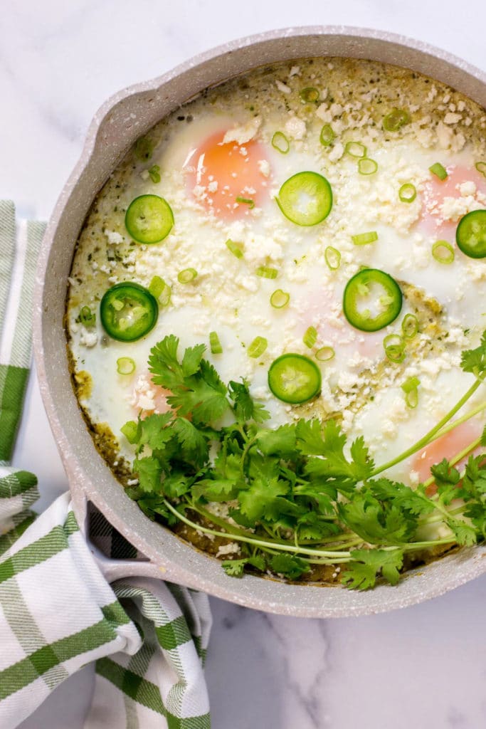 Overhead view of a skillet with baked eggs garnished with cilantro and sliced jalapenos