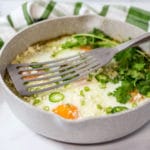 A spatula in a pan of baked eggs garnished with sliced jalapenos and cilantro