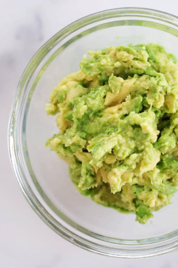 Overhead view of a clear bowl of smashed avocado