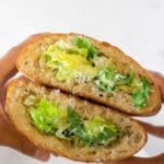 Fingers holding two halves of a ciabatta loaf cut in half, hollowed out, and filled with caesar salad