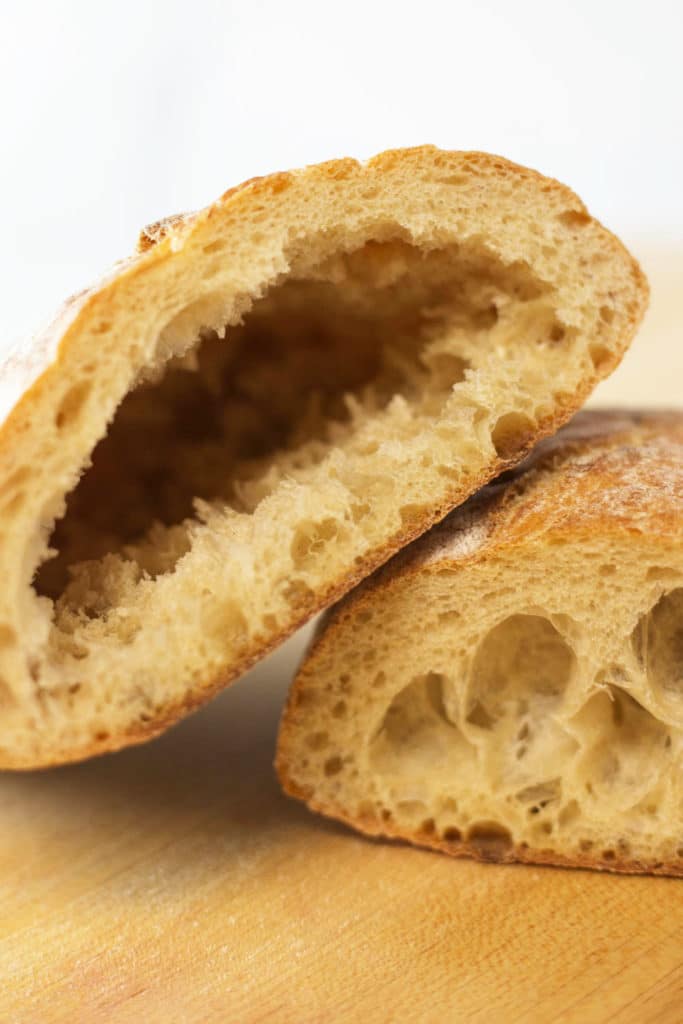 A ciabatta roll cut in half, one side leaning on top of the other, one side has a hollow center