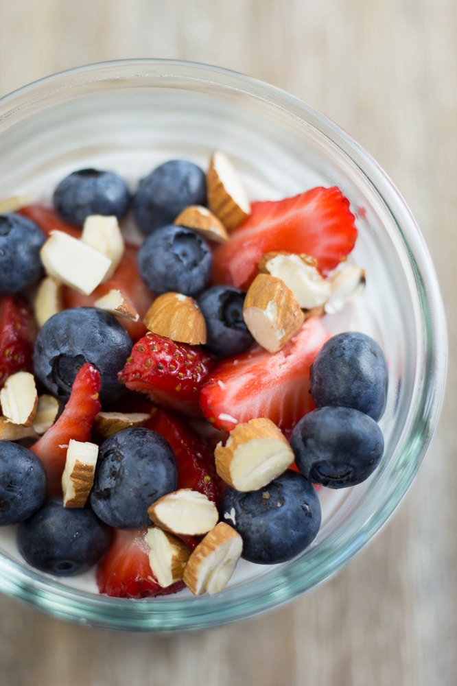 Overhead view of a clear jar of chia pudding topped with strawberries, blueberries, and sliced almonds