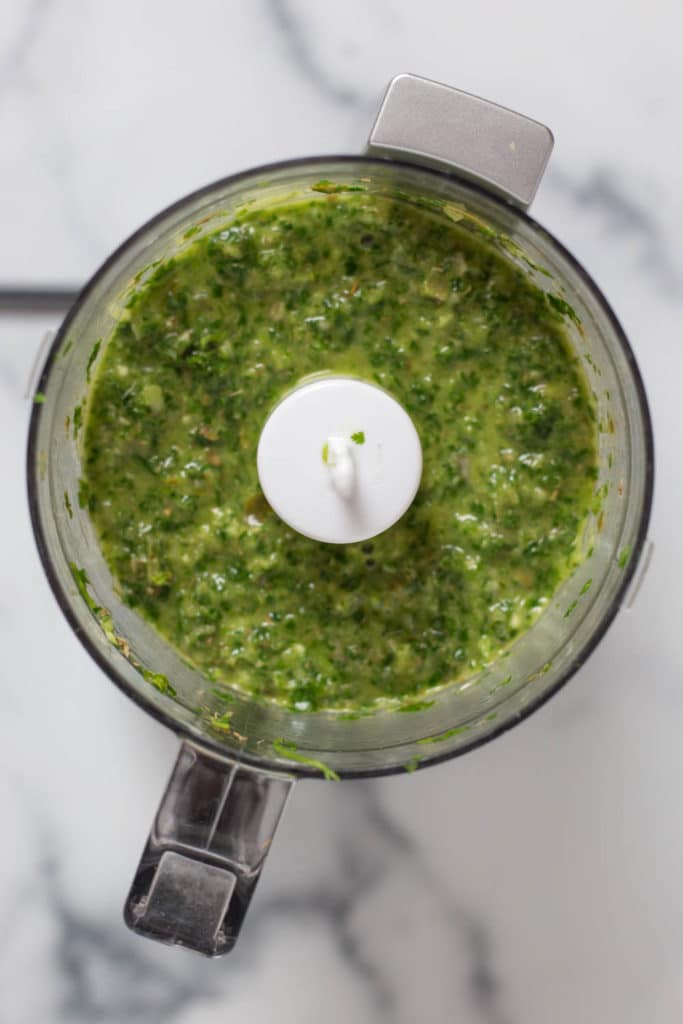Overhead view of a food processor filled with green chimichurri sauce