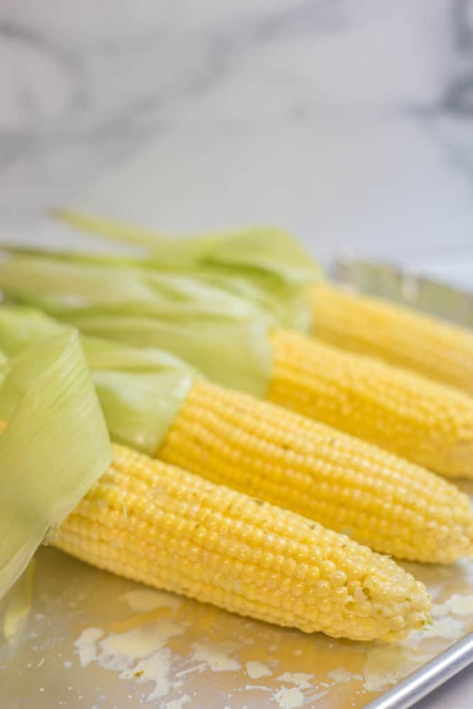 4 ears of shucked corn on a baking sheet