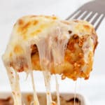 A silver spatula lifting a piece of lasagne from a white baking dish