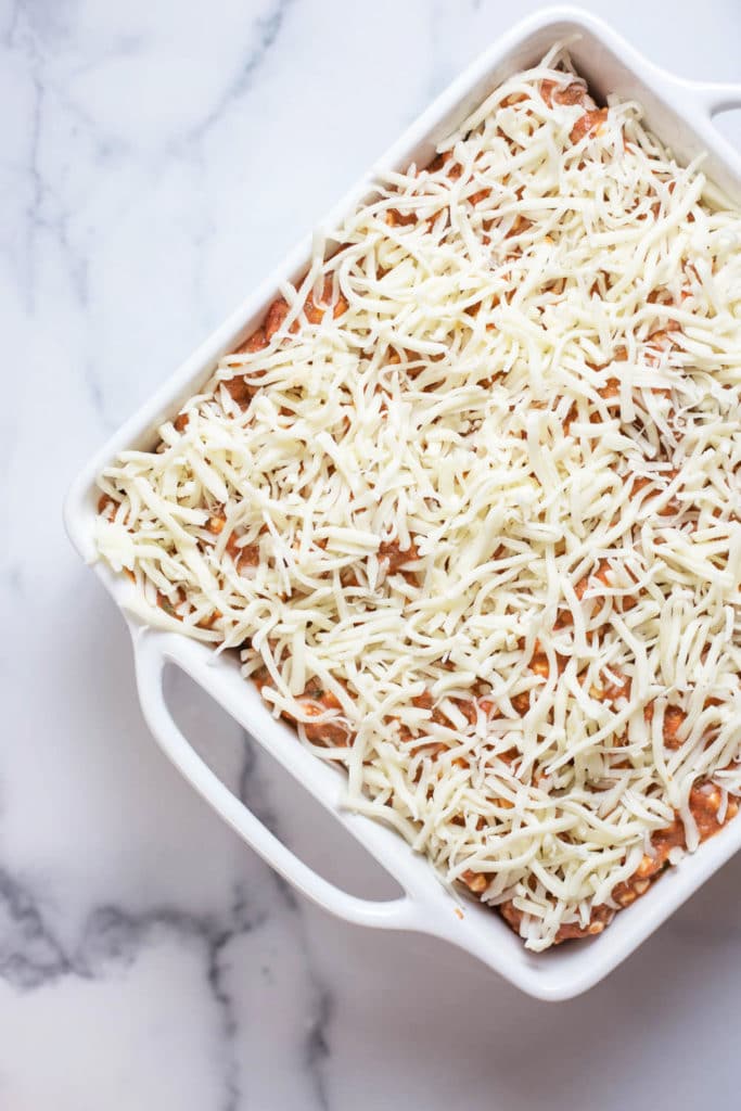 Overhead view of a white baking dish of lasagna topped with grated mozzarella cheese
