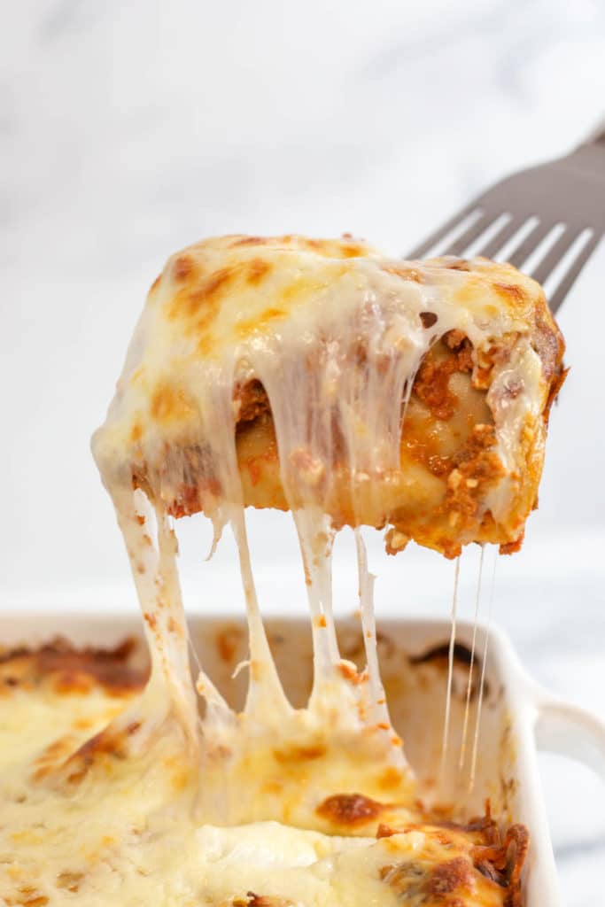 A silver spatula lifting a piece of lasagna from a white baking dish