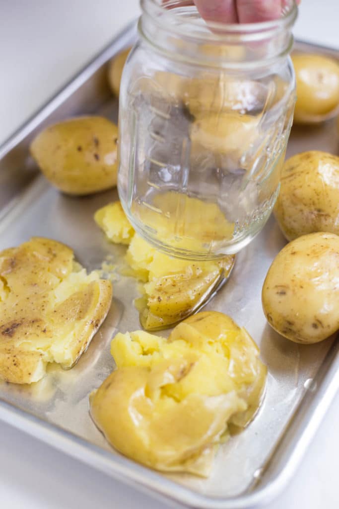 A mason jar being held over a baking sheet of baby yukon gold potatoes