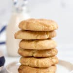 A stack of 6 snickerdoodle cookies on a small round white plate with a clear bottle of milk with blue striped straws and a blue striped napkin in the background