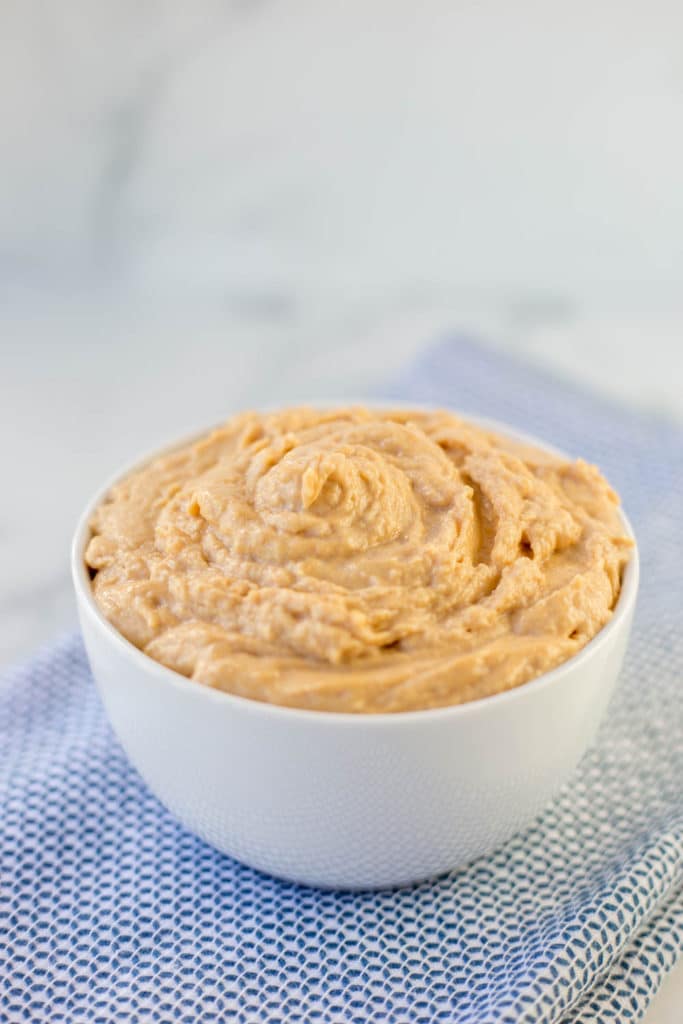 A white bowl filled with peanut butter frosting on a blue napkin