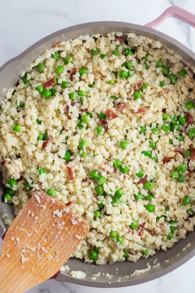 Overhead view of a skillet with cauliflower rice, peas, and bacon