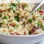 Up close view of a white bowl of cauliflower rice with peas, bacon, chives, and parmesan cheese