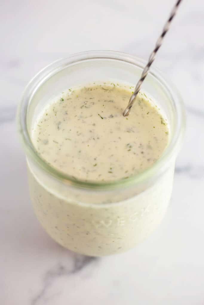 Overhead view of a clear jar of ranch dressing with a silver spoon