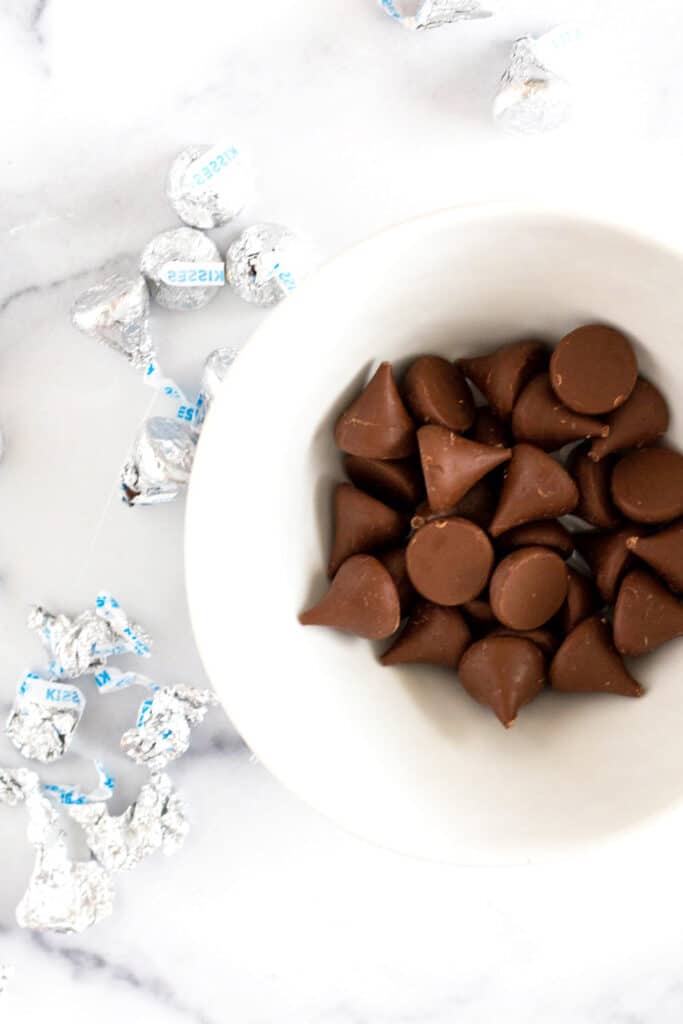 Overhead view of a bowl of unwrapped Hershey Kisses next to silver wrappers