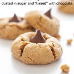 Three peanut butter kiss cookies on a white background next to cookie crumbs