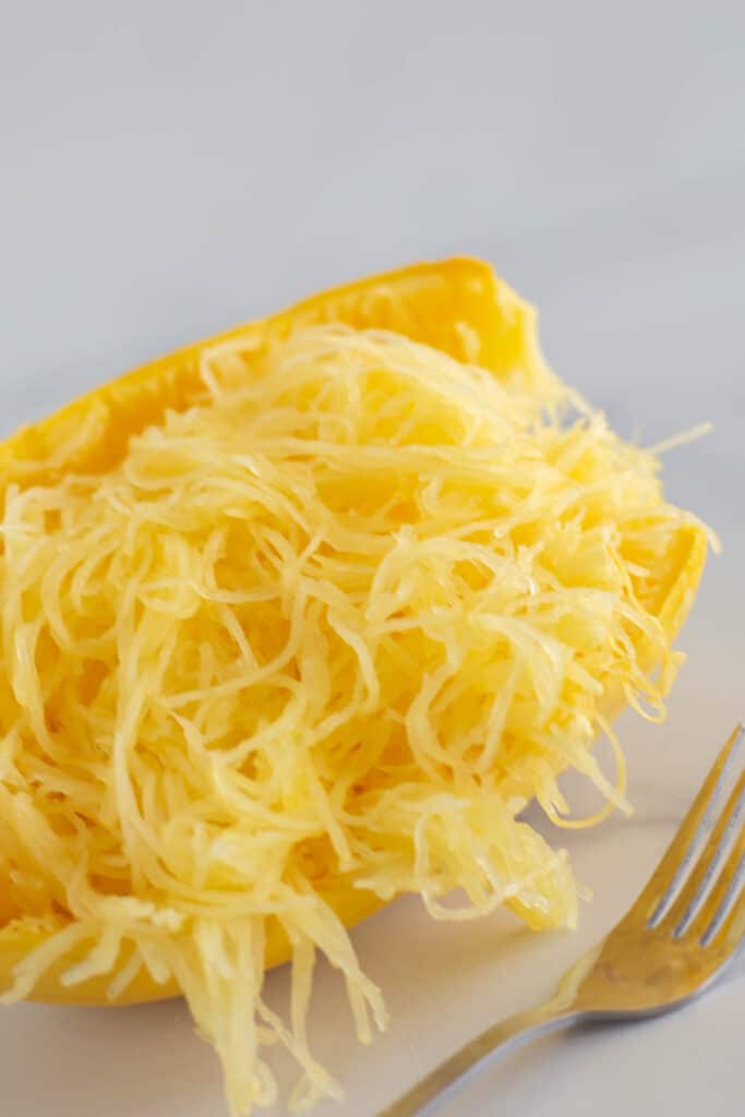 Half of a spaghetti squash pulled into ribbons next to a fork