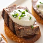 Crostini topped with steak and white sauce on a white plate