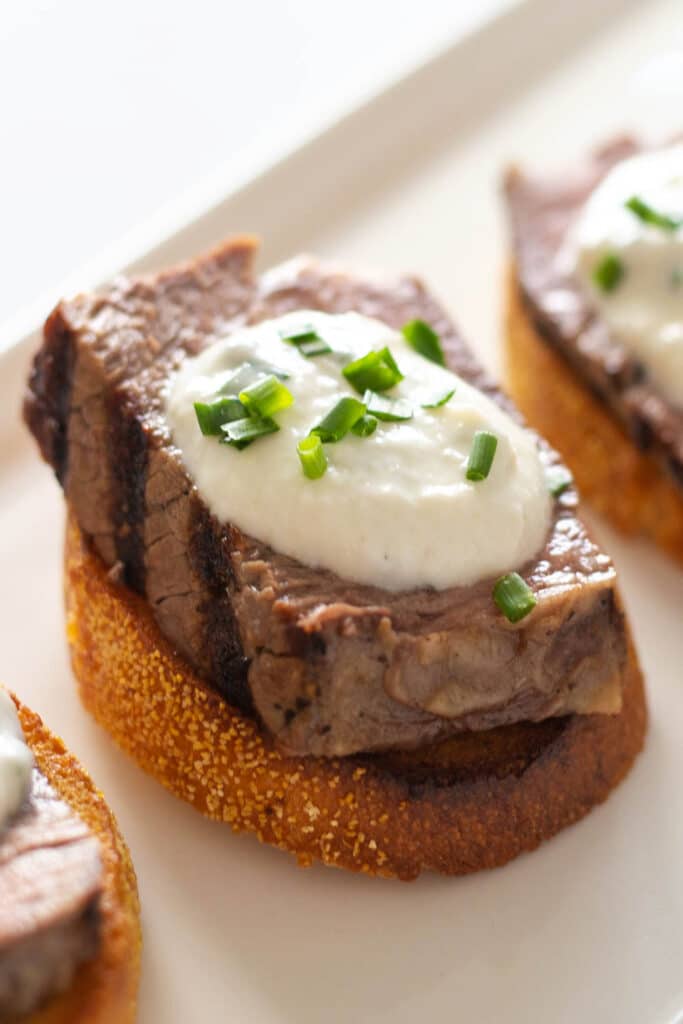 Crostini topped with steak and white sauce on a white plate