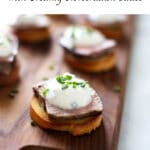 Crostini topped with steak and white sauce on a wood cutting board