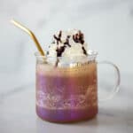 Clear coffee mug filled with chocolate frappe topped with whipped cream and a gold straw