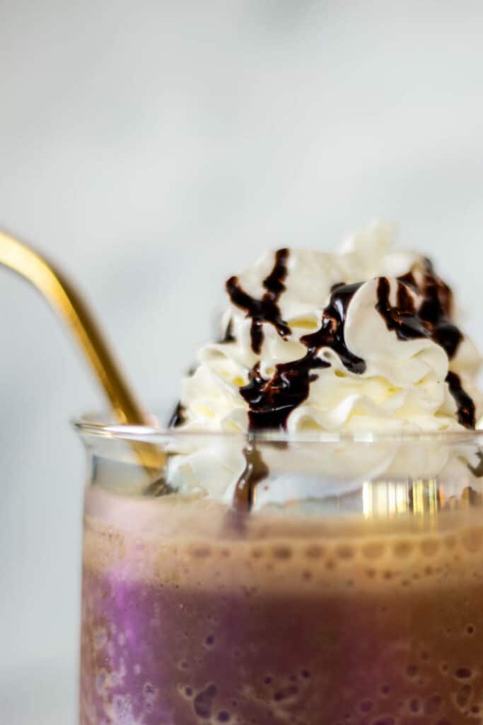 Up close shot of clear coffee mug filled with chocolate frappe topped with whipped cream and a gold straw