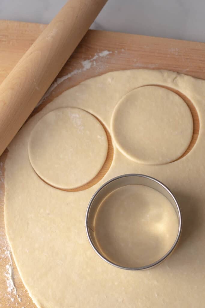 Pie crust rolled out on a cutting board with a biscuit cutter and a rolling pin